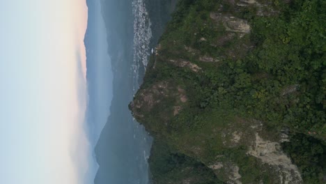 drone portrait view in guatemala flying in front of a green mountain surrounded by volcanos on a cloudy day in atitlan