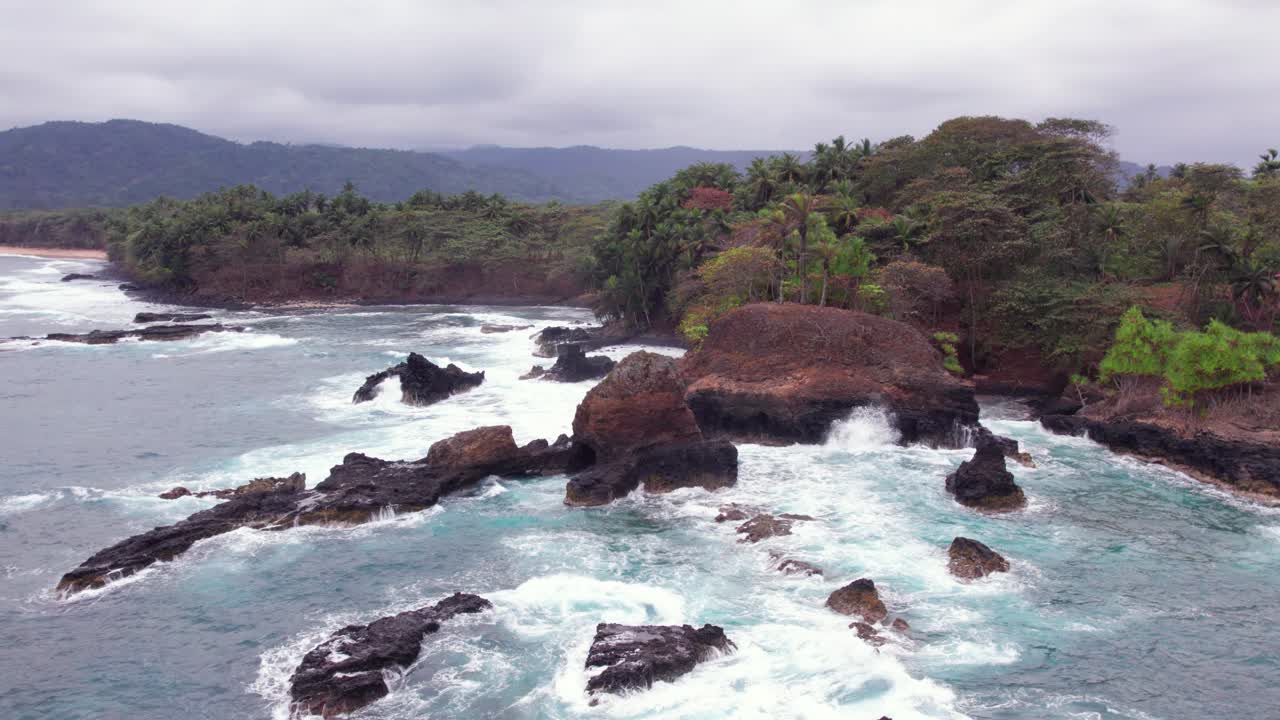 Stormy waves crash on Praia Piscina, São Tomé, a dramatic blend of wild ocean power and serene tropical beach landscape