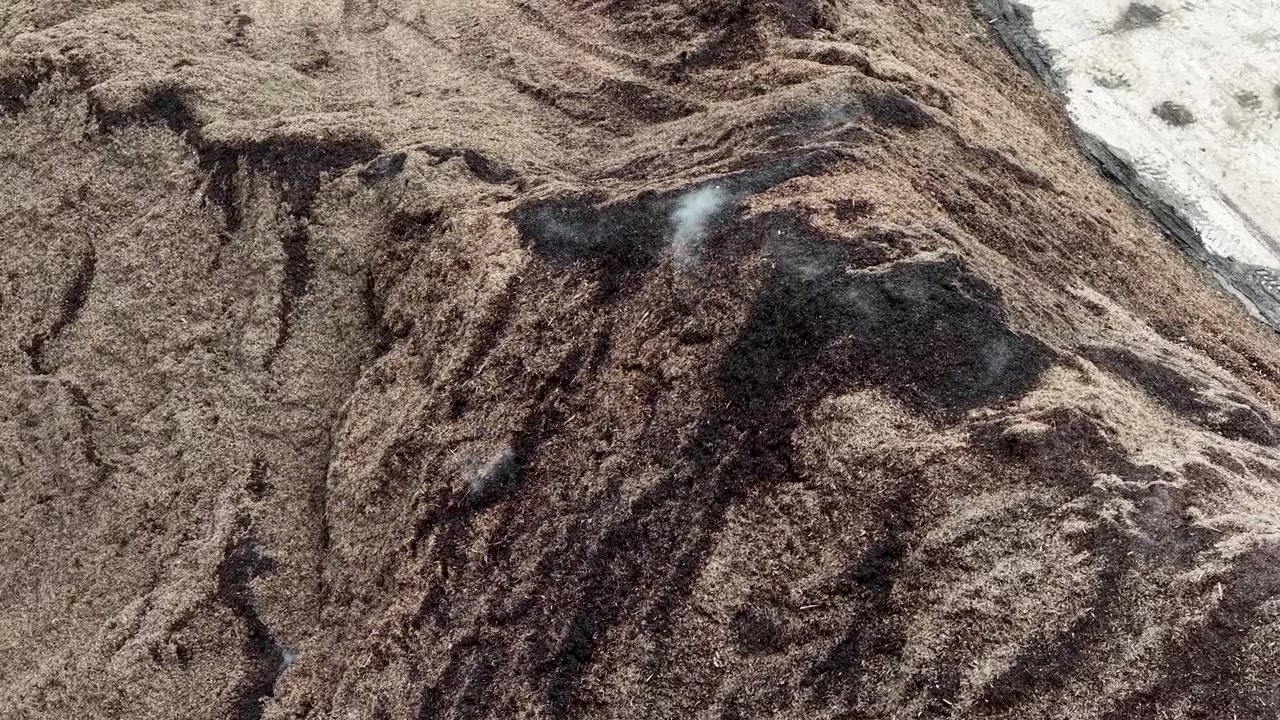 Top down drone view of tire tracks surrounding a dark material pile on the quarry floor