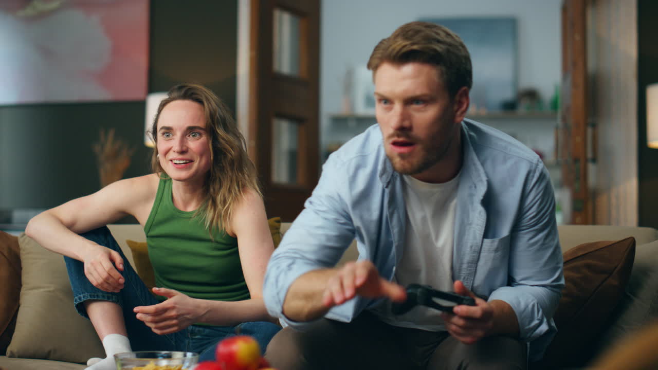 Excited couple competing videogame at home. Nasty man taking gamepad from woman