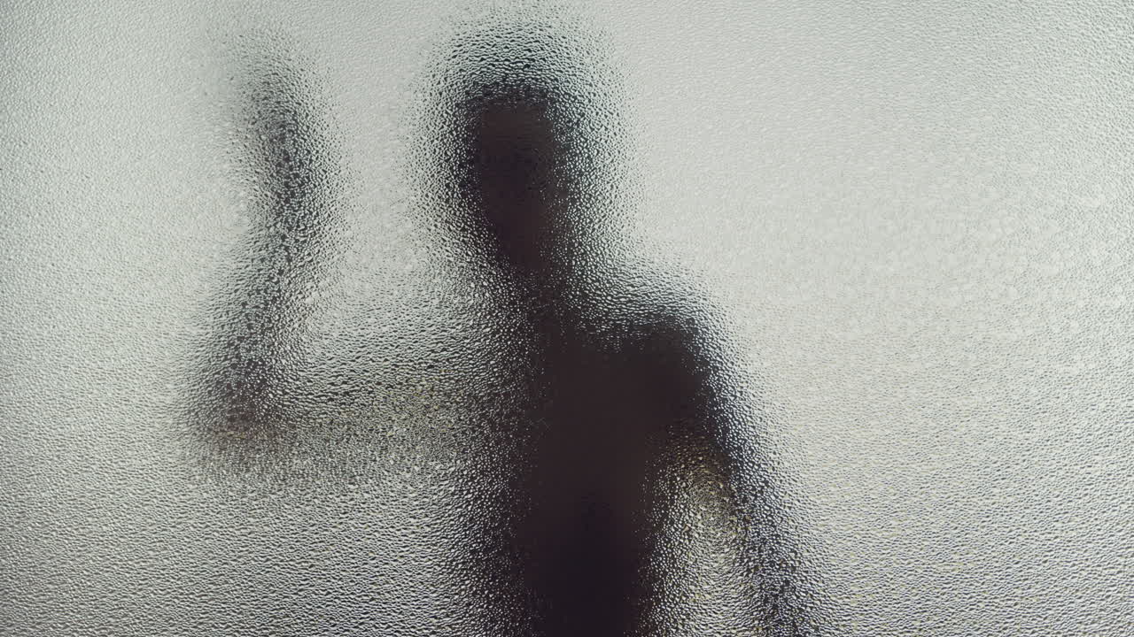 A female silhouette behind the frosted window dances slowly