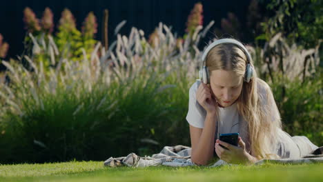 a teenager with a smartphone and headphones lies on the grass in the park