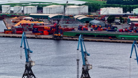 colorful containers, cranes, and bulk materials near large fuel storage tanks at riga’s port. riga, latvia