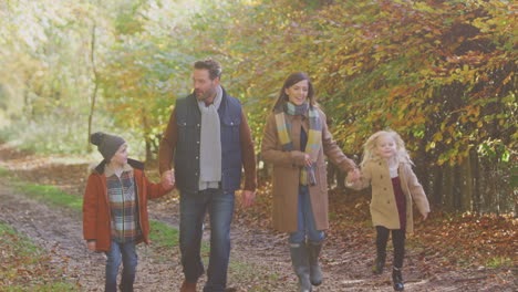 family with mature parents and two children holding hands walking along track in autumn countryside