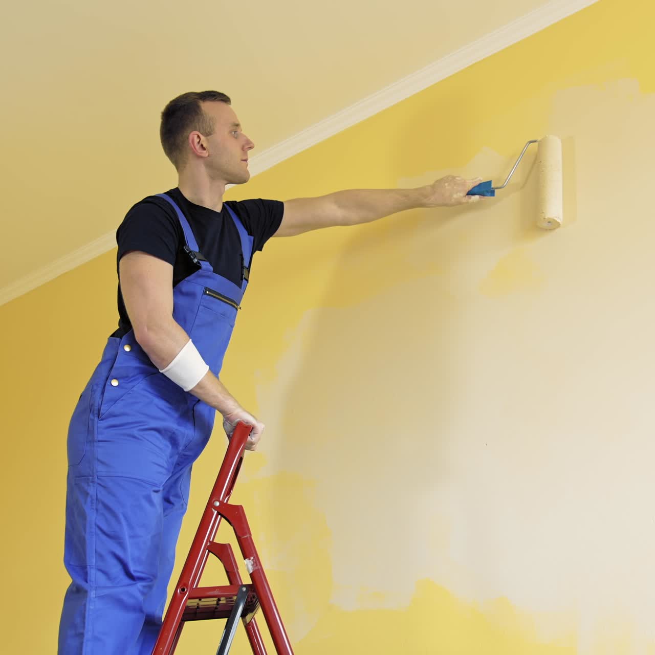Young painter doing house renovation. Handsome worker painting new wall