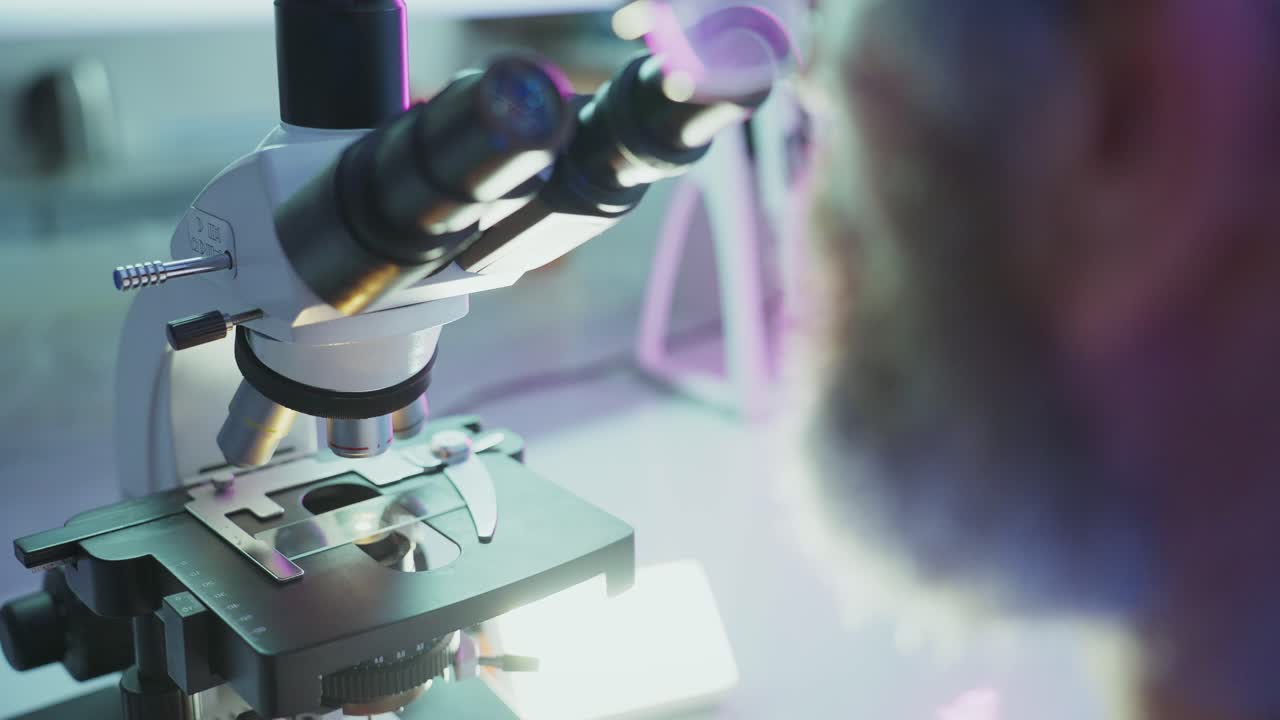 Scientist Adjusting Microscope and Looking Through Eyepieces in a Lab