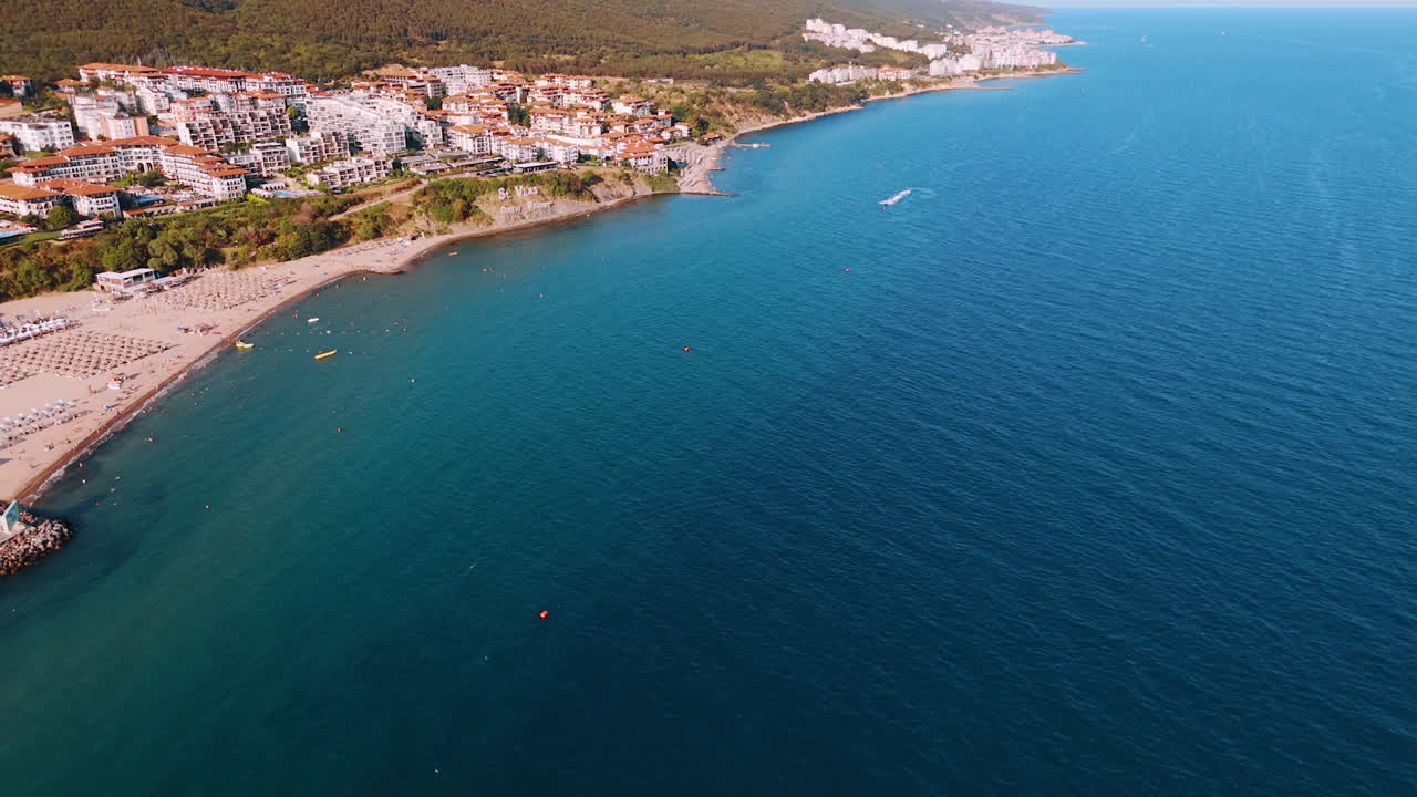 Footage over the blue waterscape of the Black Sea. People swim at the shore with sandy beach. Aerial perspective on the multiple hotels of Sveti Vlas, Bulgaria