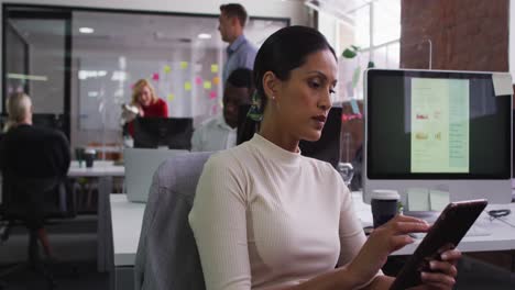 Mixed-race-businesswoman-sitting-at-desk-in-open-space-using-tablet-smiling