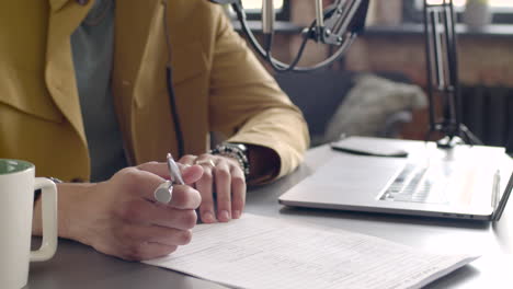 African-american-man-hands-taking-notes-on-a-table-with-laptop-and-microphone.-The-man-is-recording-a-podcast