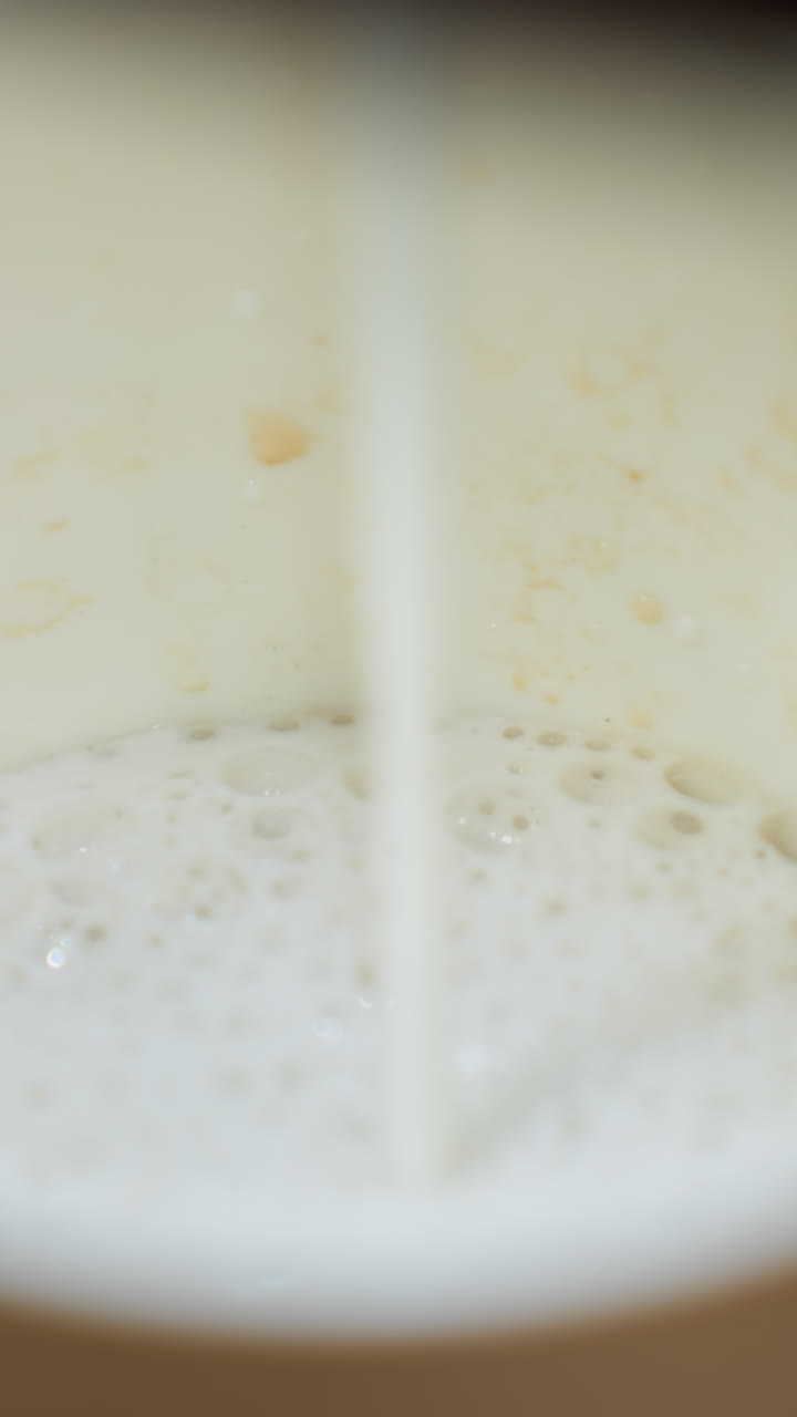 vista de cerca de la leche que se vierte en una taza de café desde una máquina de café. el video captura el momento preciso de la corriente de leche golpeando la taza, enfatizando los detalles de la leche espumosa