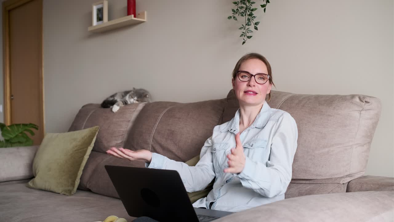 Kvinne på sofaen med videosamtale og en katt som hviler i bakgrunnen