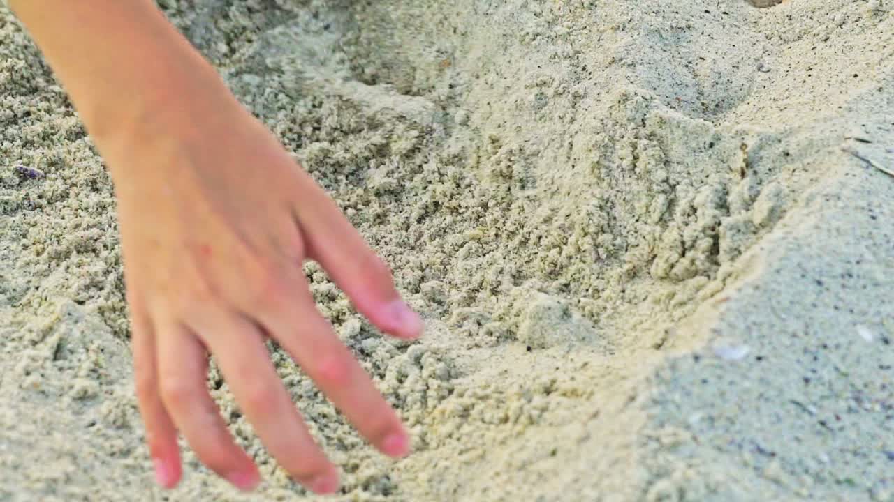 A child digs a pit with his hands in the sand near the sea on vacation. Entertainment at the beach.