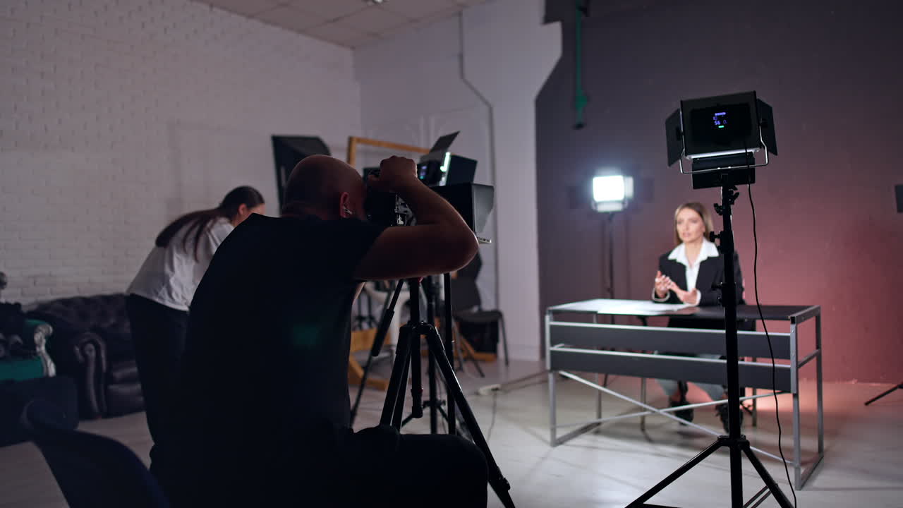 Bald bearded photographer filming a lady sitting at desk. Program, podcast or blog content footage.