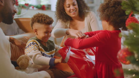 family exchanging and opening gifts around christmas tree at home