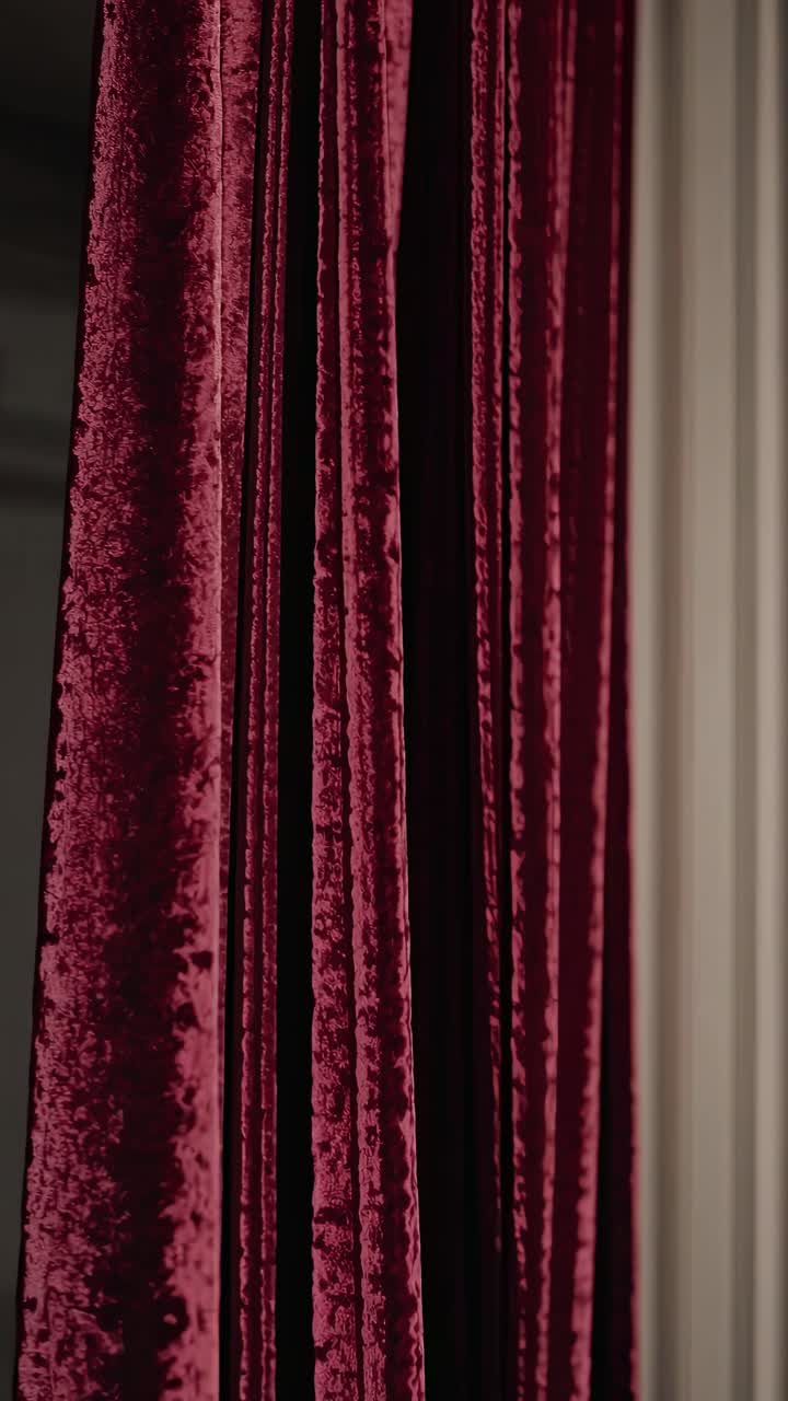 Close-up video of luxurious red velvet curtains, captured from a side angle, highlighting texture