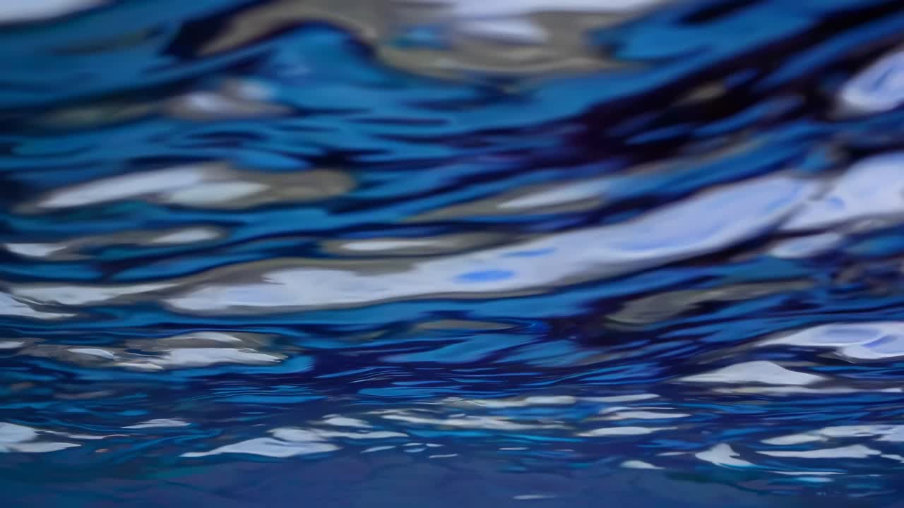 The video captures mesmerizing, abstract reflections on water, showcasing fluid motion and vibrant