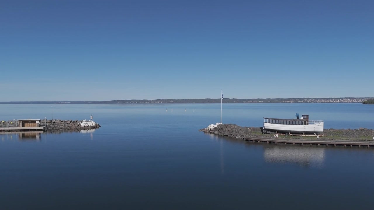 Veduta aerea con drone di moli portuali che si estendono in acque calme a Portree Harbour sull'Isola di Skye, che cattura un tranquillo paesaggio costiero sotto un cielo azzurro limpido