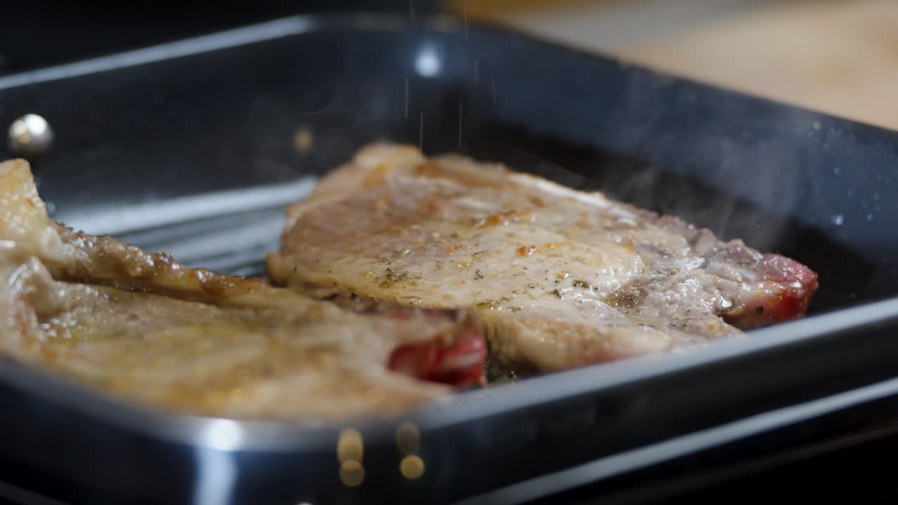 Juicy pork chops sear in hot grill pan with visible steam and seasoning