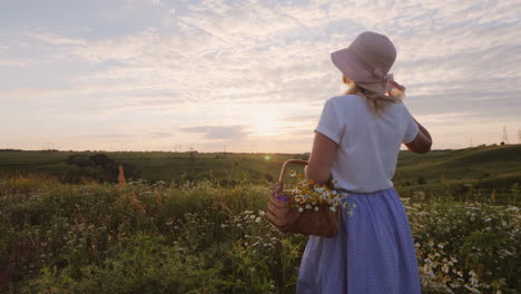 A-Middle-Aged-Woman-In-A-Hat-With-A-Basket-Of-Wild-Flowers-Stands-In-A-Meadow-Looking-Forward-To-The