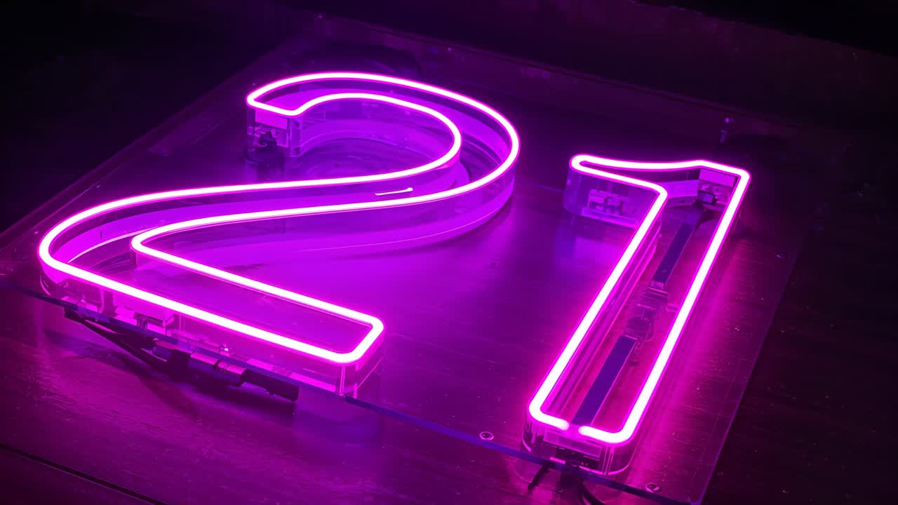 Shifting camera capturing glowing magenta 21 neon sign in dim studio on ...