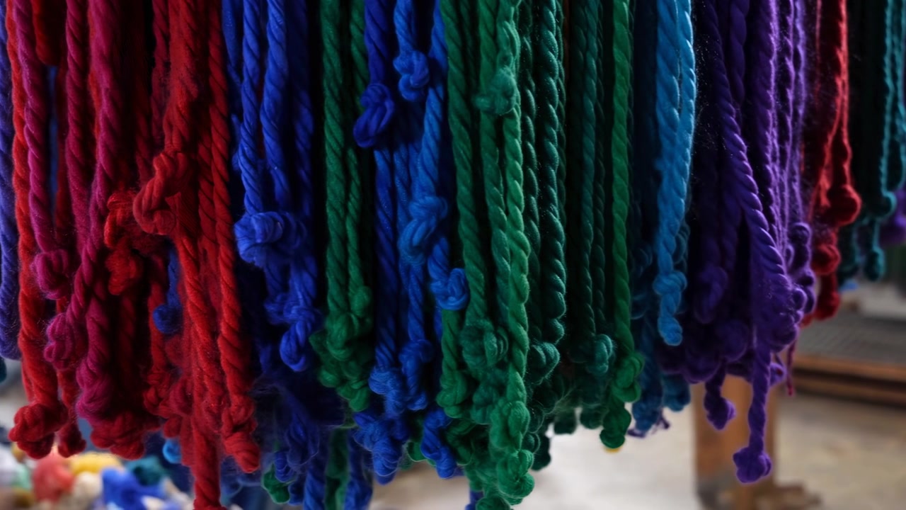 Corde di filato colorate appese in un laboratorio, tintore artigiano che ordina matasse su una rastrelliera di legno, primo piano di lana ritorta.