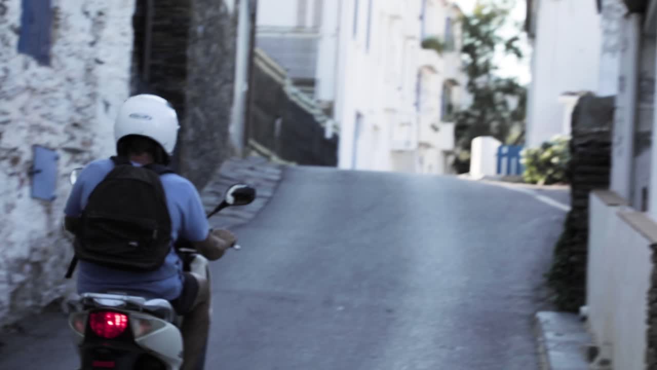 Slow motion, man riding moped scooter down European street during summer