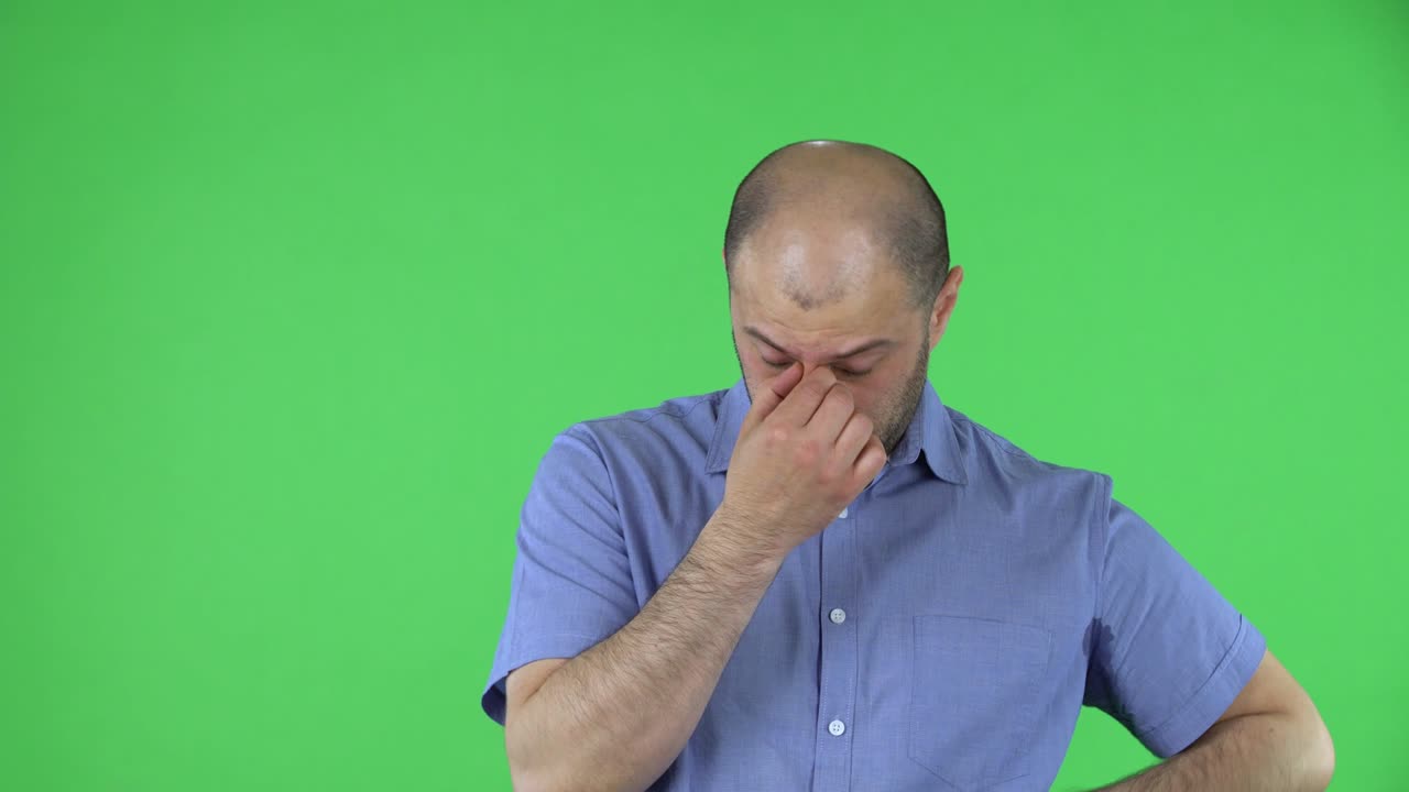 Ritratto di un uomo di mezza età turbato e stanco. Uomo calvo con barba in camicia blu in posa su schermo verde nello studio. Primo piano