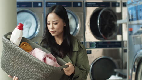 beautiful young woman carrying basket with diry clothes and abstergent while coming to laundry service