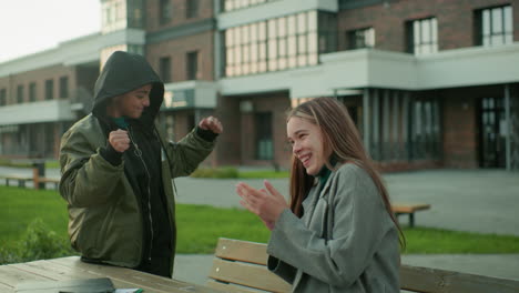 little boy launches paper kite but it unexpectedly flies back toward his head, making his sister burst into laughter while he claps hands in playful embarrassment during outdoor fun