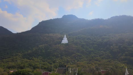 luang por khao, wat theppitak punnaram, a reverse aerial footage of the famus white temple on the mountain revealing a communication antenna and stairway up shrine, and partly the complex