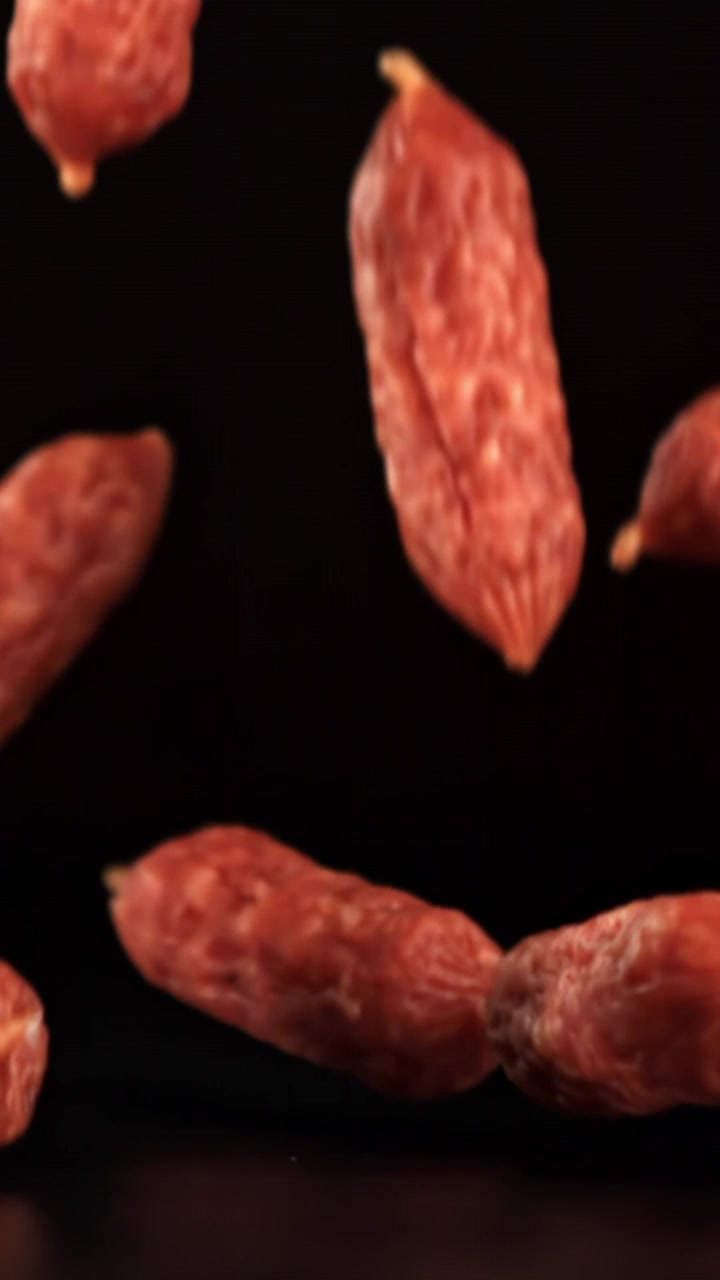 Mini salsicce di salame che cadono al rallentatore su sfondo nero.