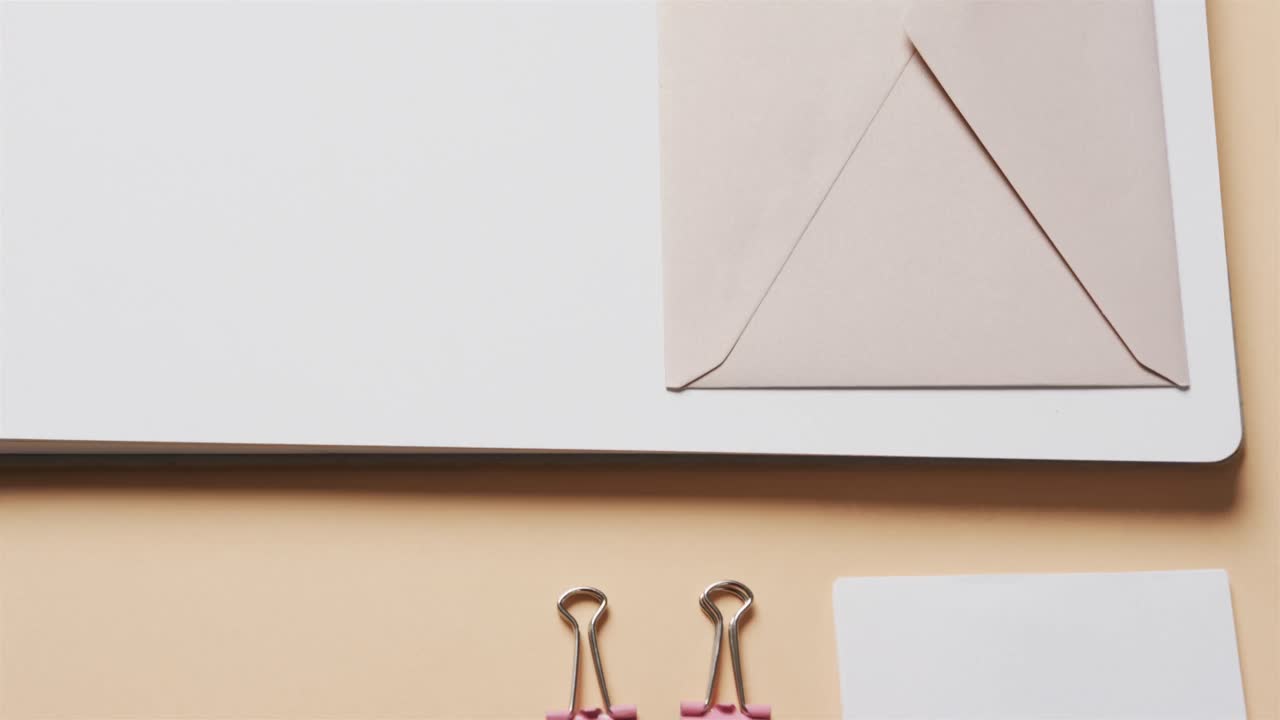 primer plano de cuadernos, bolígrafos y papelería dispuestos sobre un fondo beige, en cámara lenta