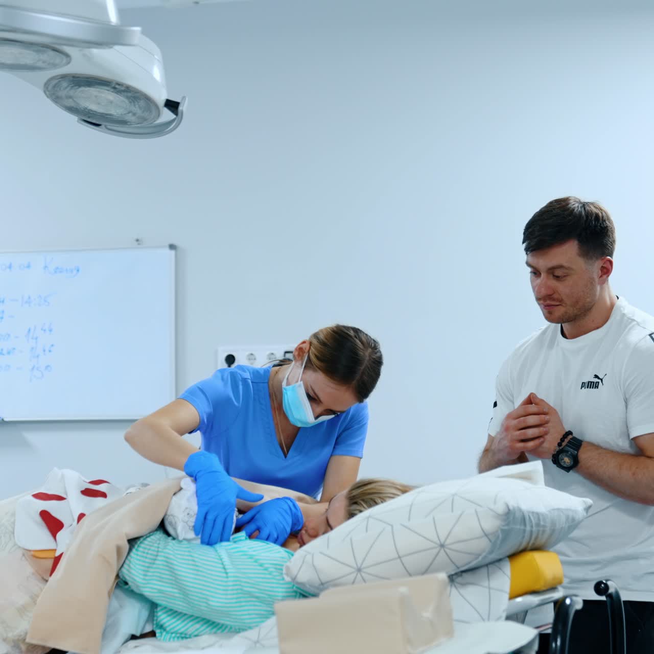 Female medic is helping mom to breastfeed her baby for the first time. Father is standing beside watching