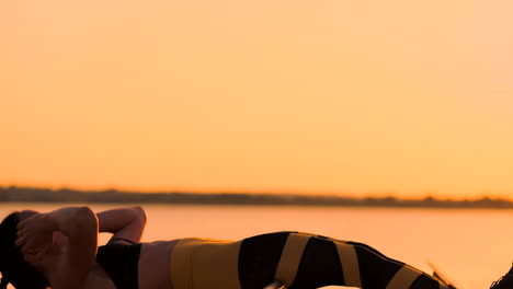 ejercicios de músculos abdominales. una joven belleza atlética al atardecer contra el lago en verano mujer en ropa deportiva haciendo ejercicios para los abdominales en cámara lenta en la barra