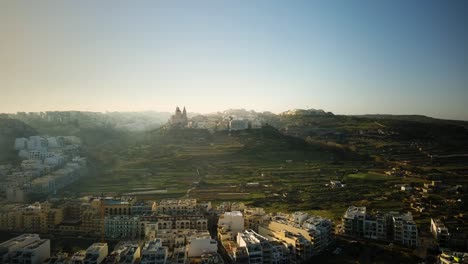 Drone-shot-flying-towards-Mellieha-Church-on-a-hill-in-a-heavily-misty-morning-in-Malta-from-far-away