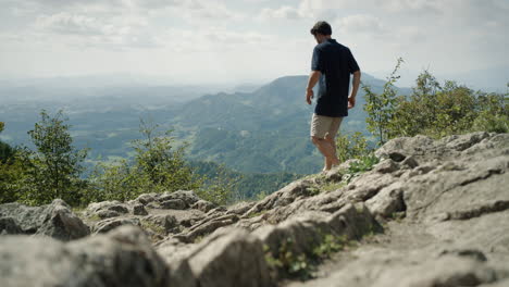 man in dark shirt and light shorts walking down the rocks to the viewing point to see into the valley