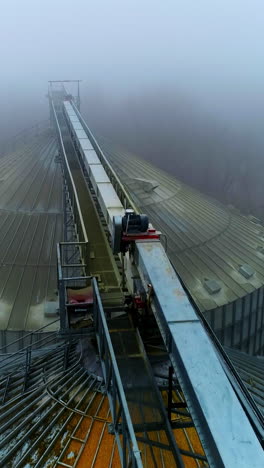 dusty tops of the bin at grain elevator complex. drone footage above the metal tanks at modern agricultural plant. foggy weather backdrop. vertical video