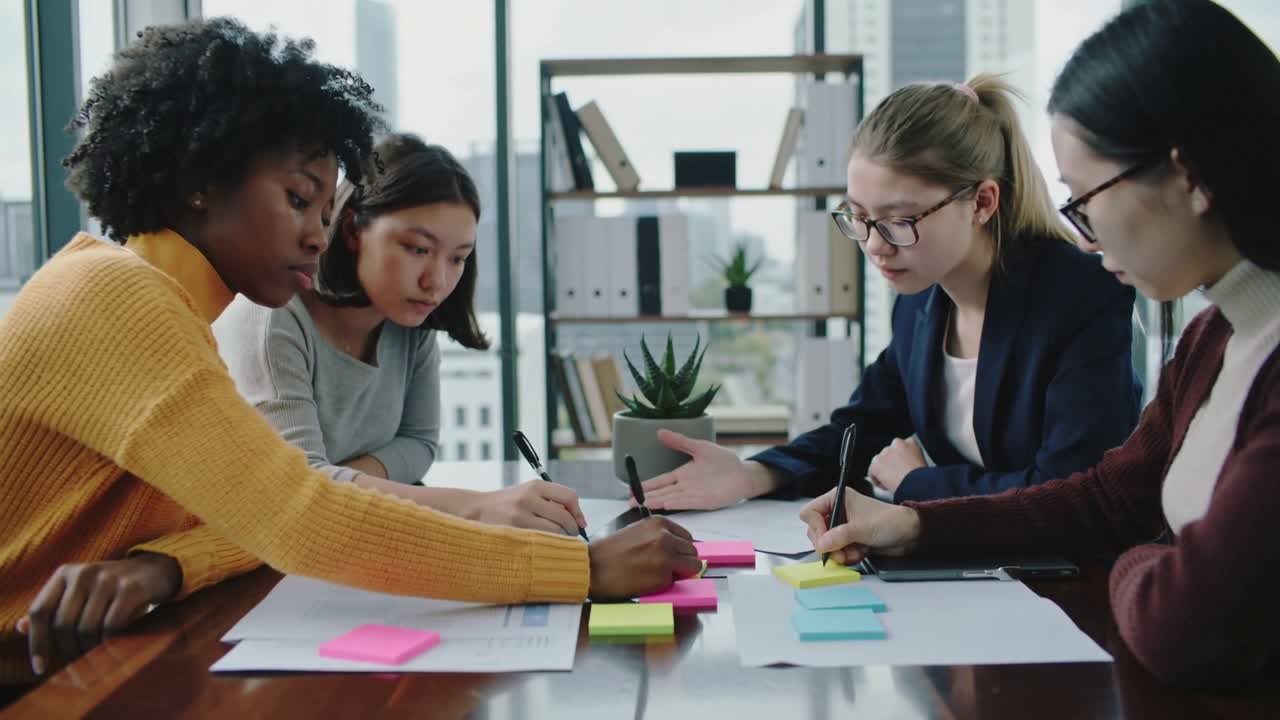 Reaching leftmost woman in mustard sweater placing sticky notes in meeting room team planning tasks