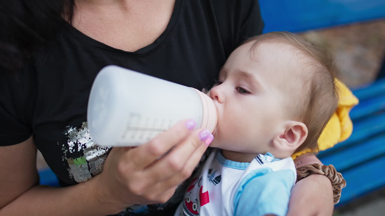Sweet baby suckling milk from bottle. Lovely child lying in mom's hands and having some meals. Close up.