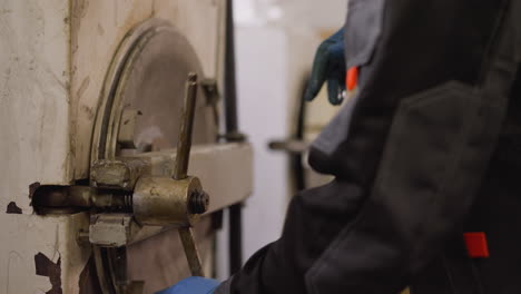 worker in protective gear manually operating kiln hatch in a ceramic workshop, focus on hand with lever