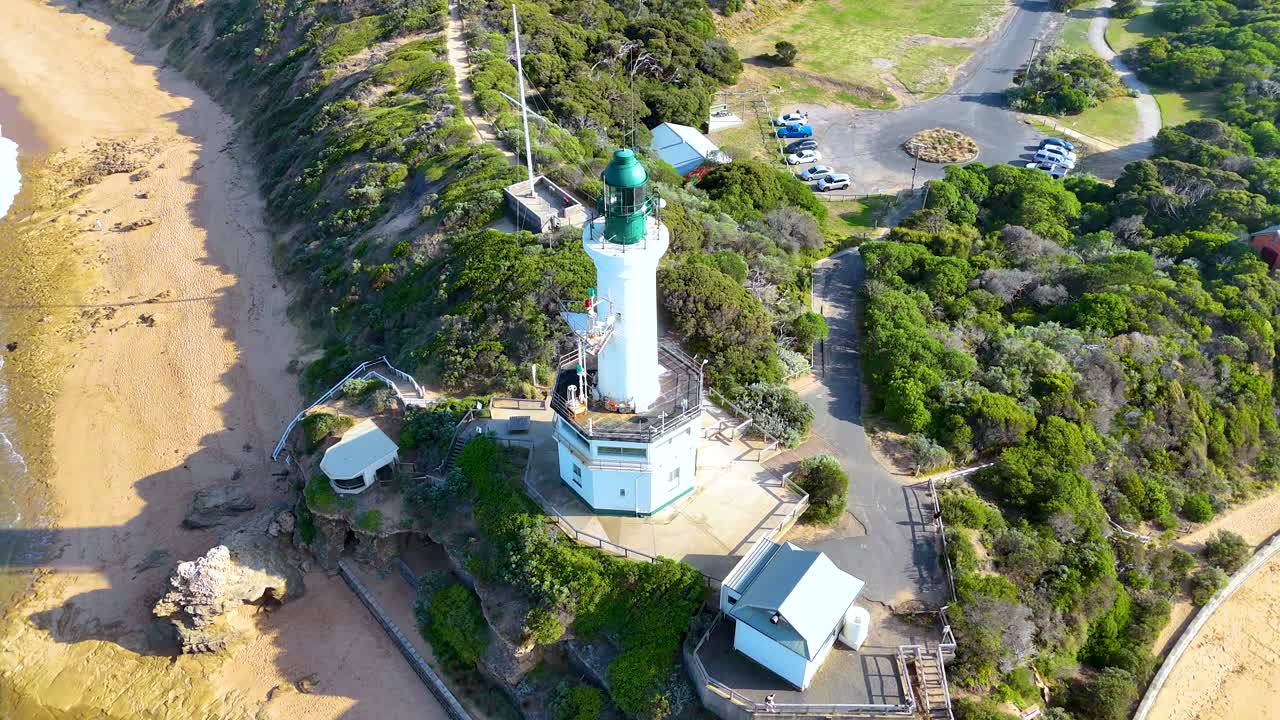 Aerial footage captures Point Lonsdale Lighthouse, surrounded by lush greenery and a sandy beach under bright daylight