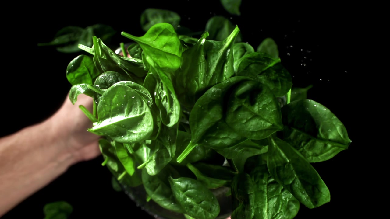 Foglie di spinaci freschi che cadono in uno scolapasta con goccioline d'acqua
