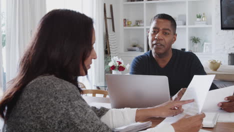 hombre afroamericano de mediana edad con una computadora portátil dando consejos financieros a una mujer durante una reunión en su casa