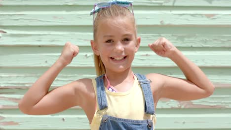 Portrait-of-happy-caucasian-girl-pumping-arms-over-beach-house