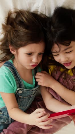 two young girls lying on a bed using a smartphone