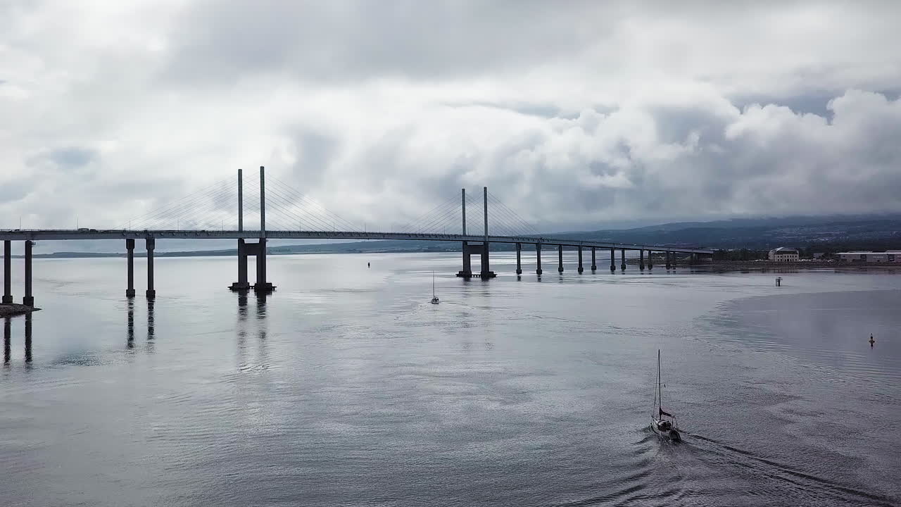 Aerial view of Kessock bridge with boats in the foreground on a cloudy summer day in Scotland.
