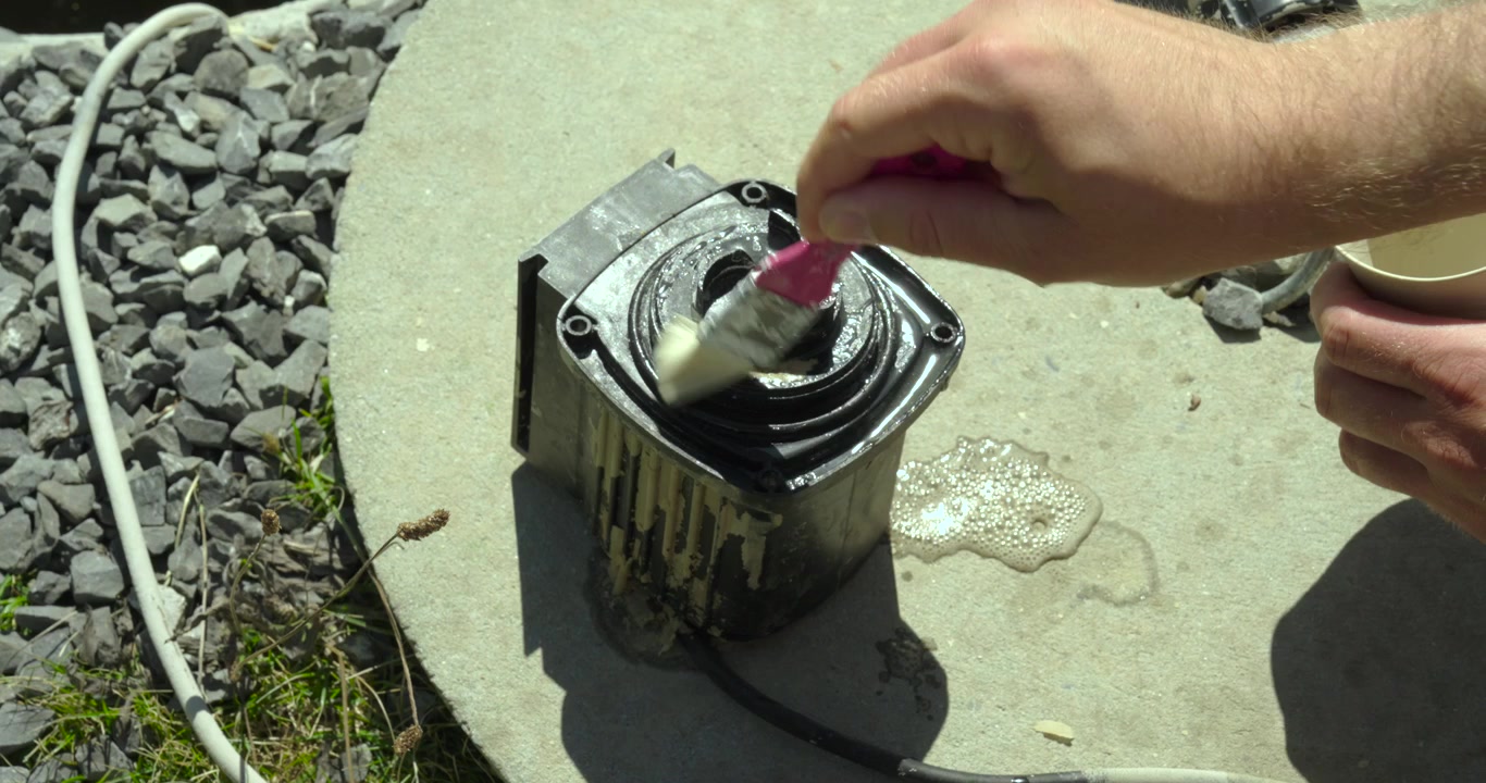 Close-up of a person applying descaling solution to a pump component with a brush during maintenance. Concept of cleaning, limescale removal, pump repair, and mechanical servicing.