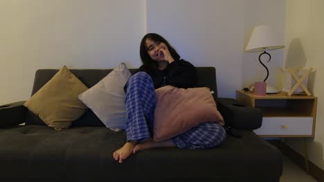 a cute, asian woman in her pajamas sitting on the couch, laughing