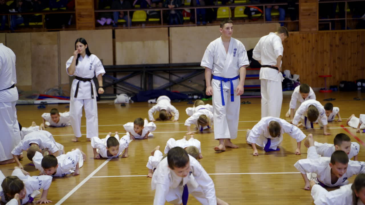 Boys and girls studying karate at the training in gym. Coaches walk and watch every young sportsman.