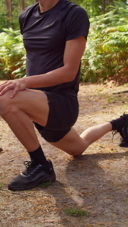 video vertical de un hombre calentándose y estirando las piernas y los pies antes de hacer ejercicio corriendo por el bosque filmado en tiempo real